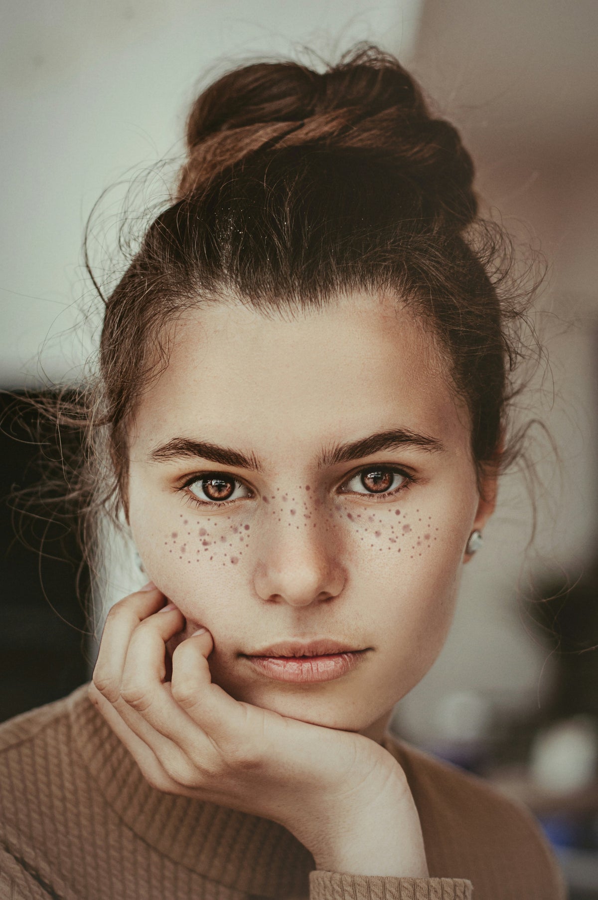 Teenage girl with freckles and her hair in buns resting her chin on her hand