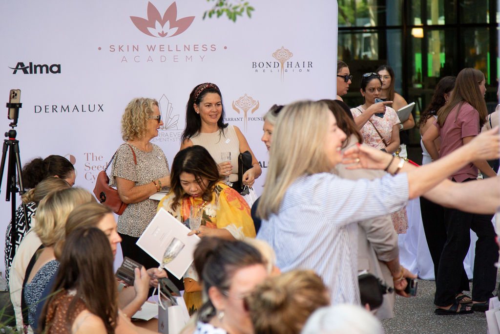 Guests mingling and taking photos in front of the Skin Wellness Academy media wall at a previous event