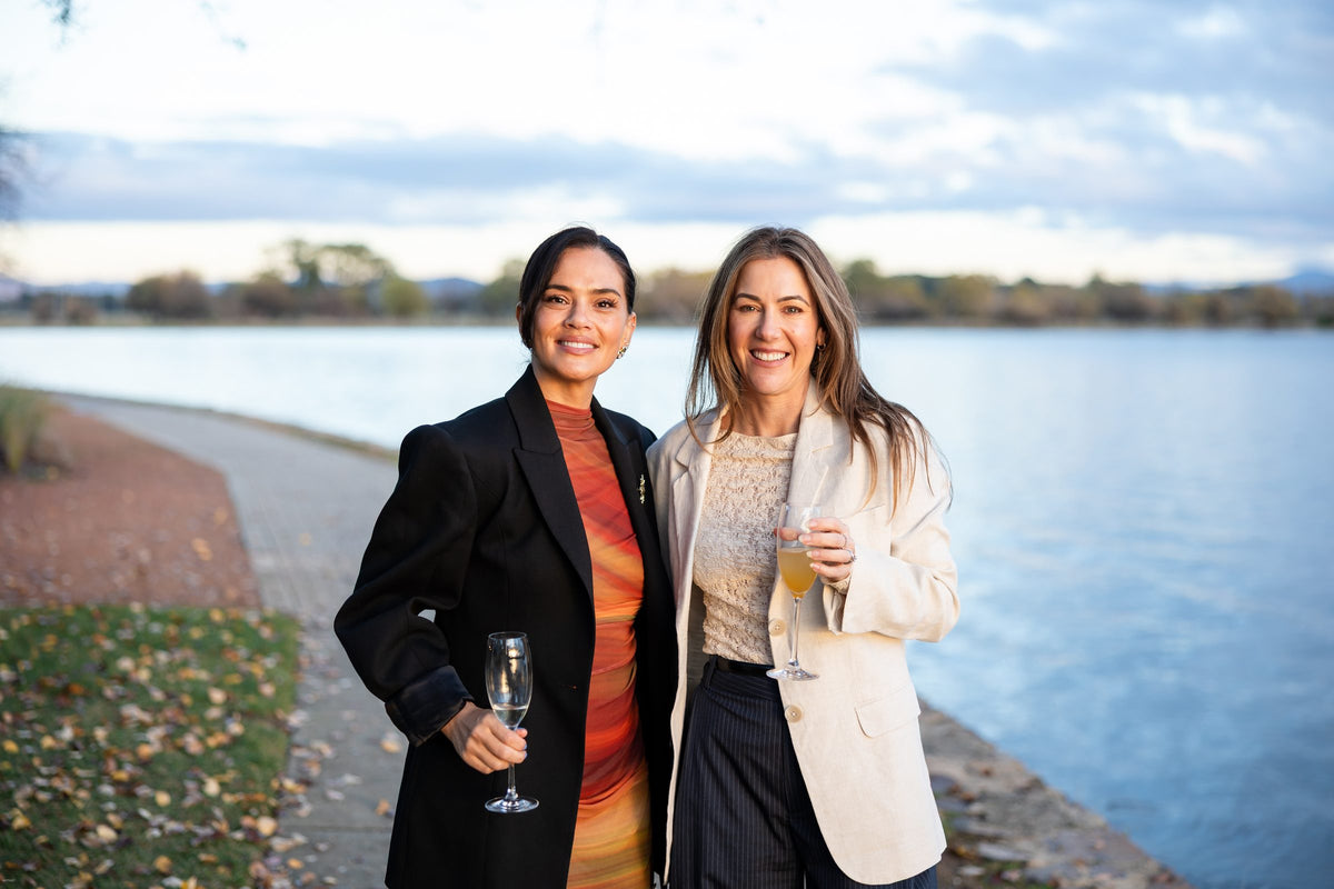 Two women smiling with drinks beside the lake at Thrive Through Change 2026 in Canberra