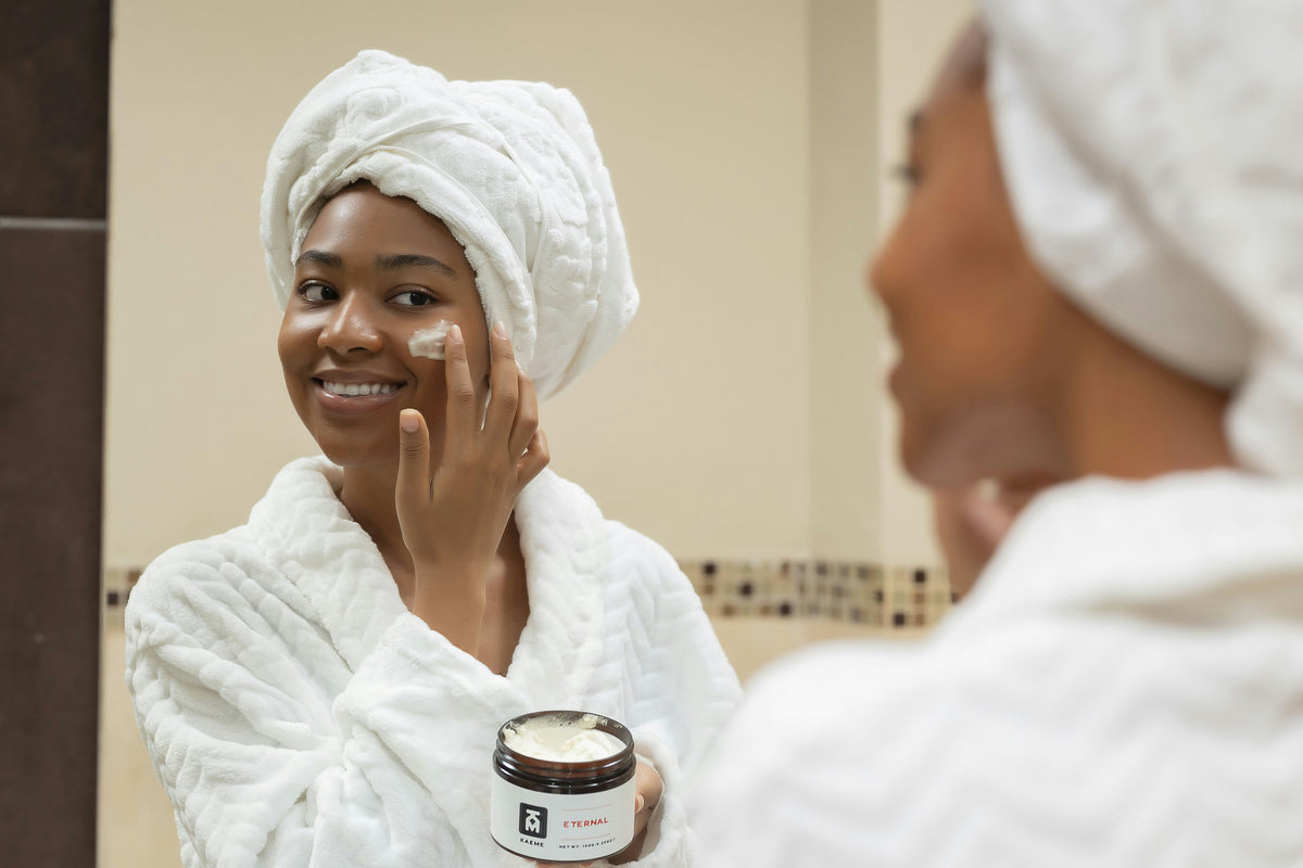 Smiling woman with her hair wrapped in a towel applying moisturiser from a jar at home
