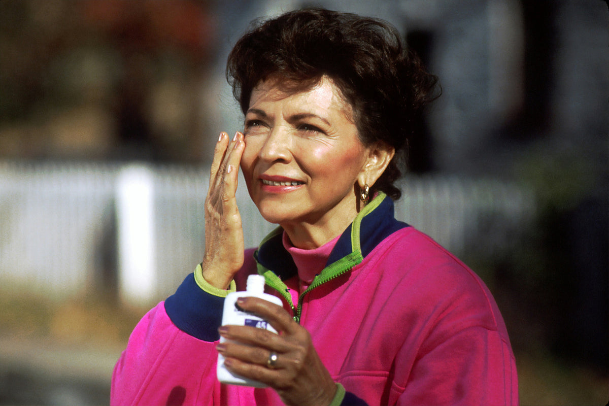 Smiling mature woman applying sunscreen to her face