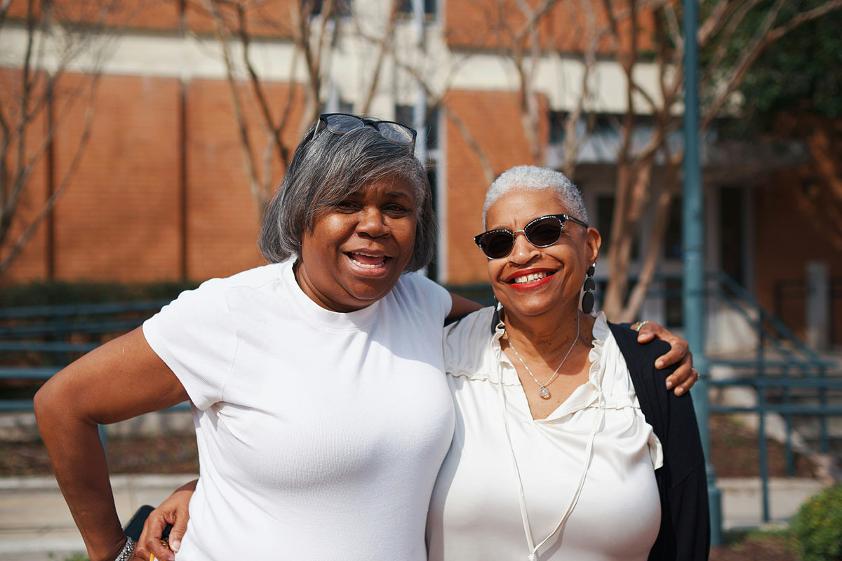 Two smiling women in their fifties and sixties standing arm in arm outdoors