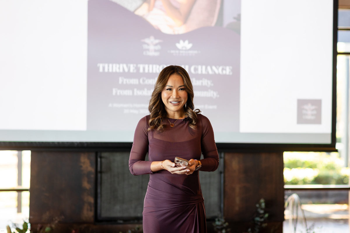 Event host in a plum dress speaking on stage in front of the Thrive Through Change presentation